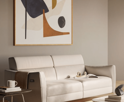 A modern living room features a beige sofa with a book and cup on it, framed by abstract art on the wall. The ambiance is cozy and minimalist.
