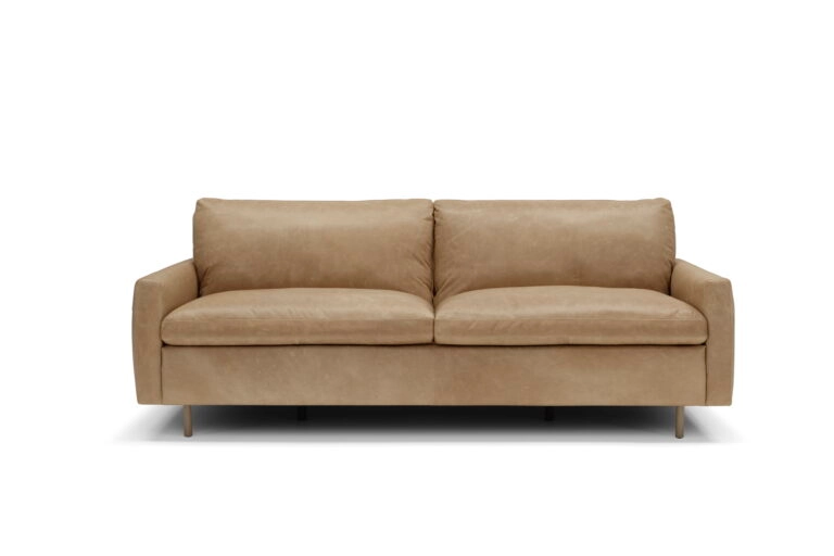 A modern living room features a white sofa with a cushion, framed by large windows showing winter trees. Nearby, lush plants and a standing lamp create a serene, elegant atmosphere.