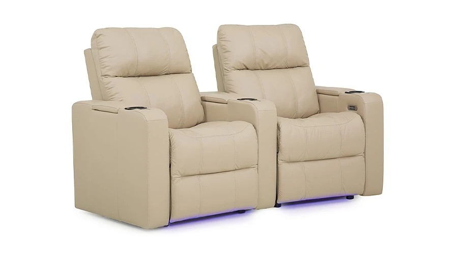 Two beige recliner chairs with plush upholstery are side by side. They feature cup holders in the armrests and have soft blue lighting underneath.