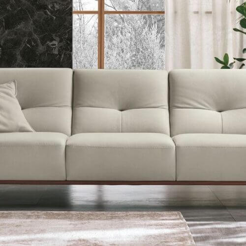 Modern living room with a sleek cream sofa, single cushion, and lush green plants. Dark marble wall and large windows create a cozy, elegant ambiance.